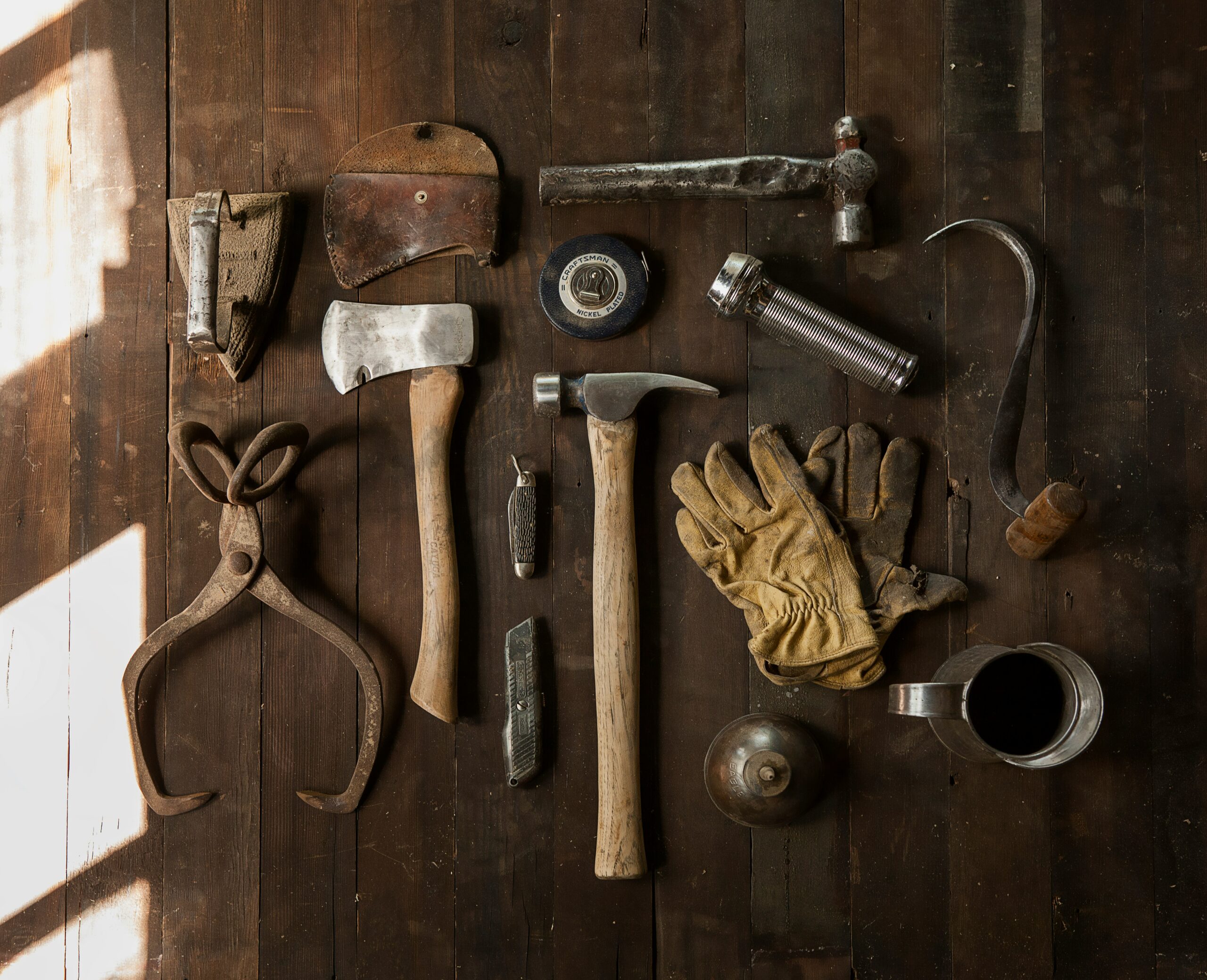 A collection of tools including a hammer on a dark wood plank background.