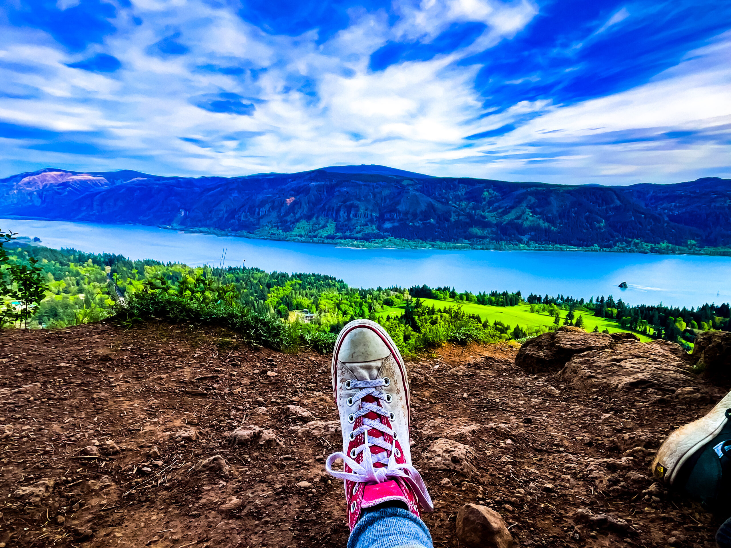 A single converse shoe looking out over a cliff with mountains and a river in the distance.